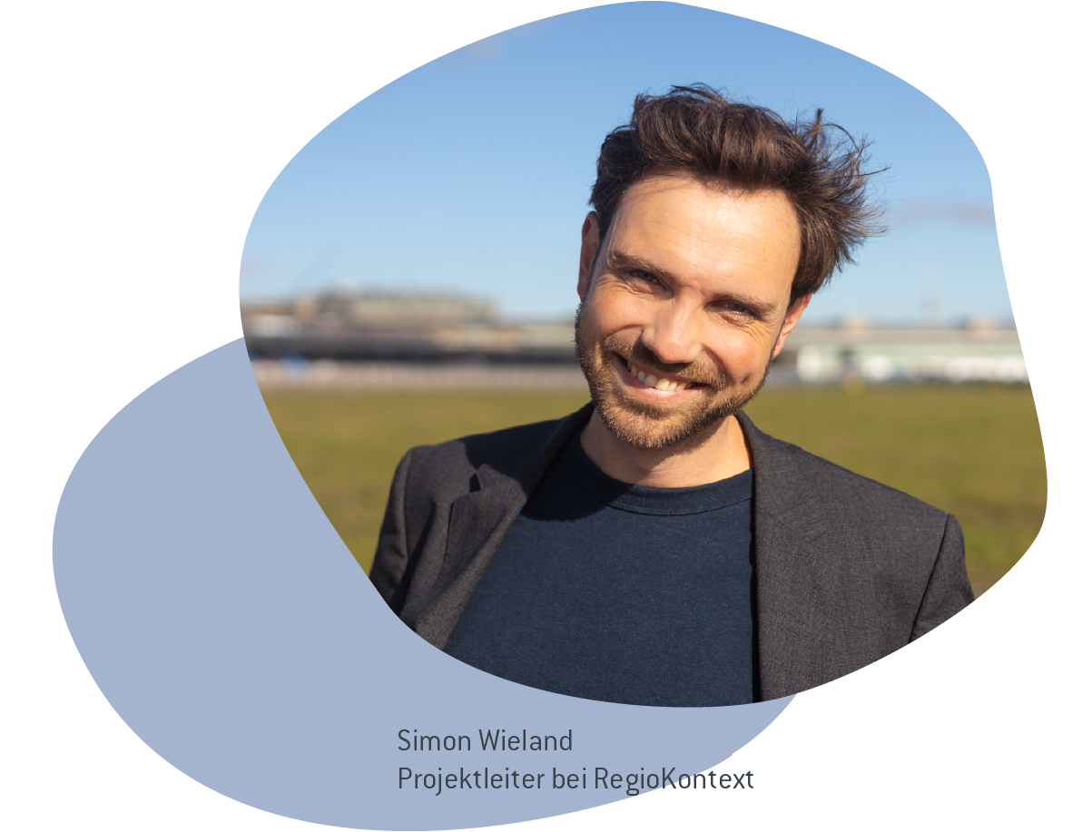 Man sieht Simon Wieland: er lächelt in die Kamera und trägt einen Blazer.